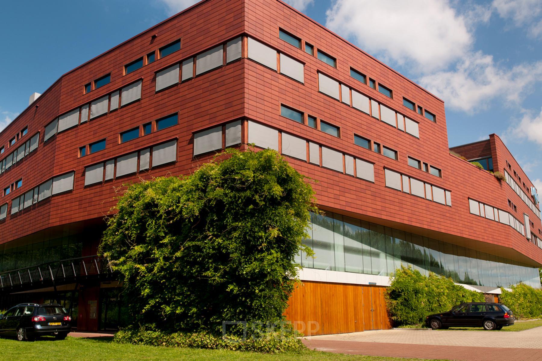Roodbruin kantoorpand aan de Multatulilaan 12 in Culemborg, met moderne architectuur en parkeergelegenheid voor het gebouw. Ideaal voor bedrijven op zoek naar een representatieve locatie om een kantoor te huren.