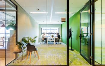 Lichte kantoorruimte in De Meern met glazen wanden en groen tapijt, twee personen werken aan bureaus bij het raam.