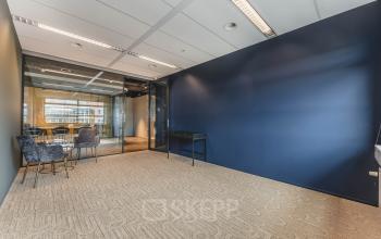 Moderne kantoorpandinterieur met glazen muur op Rijnzathe 12, De Meern. Geschikt voor het huren van flexibele kantoorruimte. De ruimte heeft een blauwe wand, stoelen en een tafel.