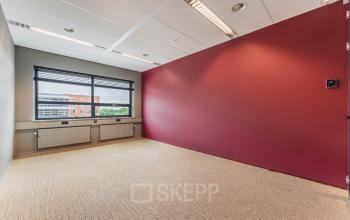 Kantoorruimte te huur in De Meern op Rijnzathe 12, met rood accentmuur en groot raam dat zorgt voor veel lichtinval. Perfecte ruimte om een eigen kantoor te creëren.