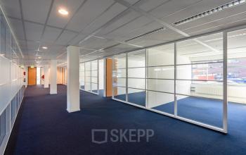 Binnenkant van een kantoorruimte op Delftechpark 17-19 in Delft met glazen wanden en blauw tapijt, ideaal voor werkruimtes of kantoren te huur.