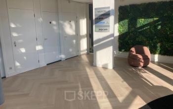 Ingang van het kantoorpand op Delftechpark 17-19 in Delft met een groene plantenwand en een comfortabele zitstoel, ideaal voor als je kantoorruimte wilt huren.