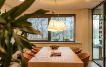 Kantoorruimte huren aan Marshalllaan 2, Delft. Moderne vergaderruimte met houten tafel en comfortabele stoelen. Grote ramen bieden veel natuurlijk licht. Ideaal voor zakelijke bijeenkomsten in kantoorpand.