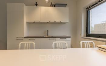 Moderne kantoorruimte in Delft met strakke keukenfaciliteiten en neutrale tinten, ideaal voor ontspanning of informele bijeenkomsten tijdens een drukke werkdag.