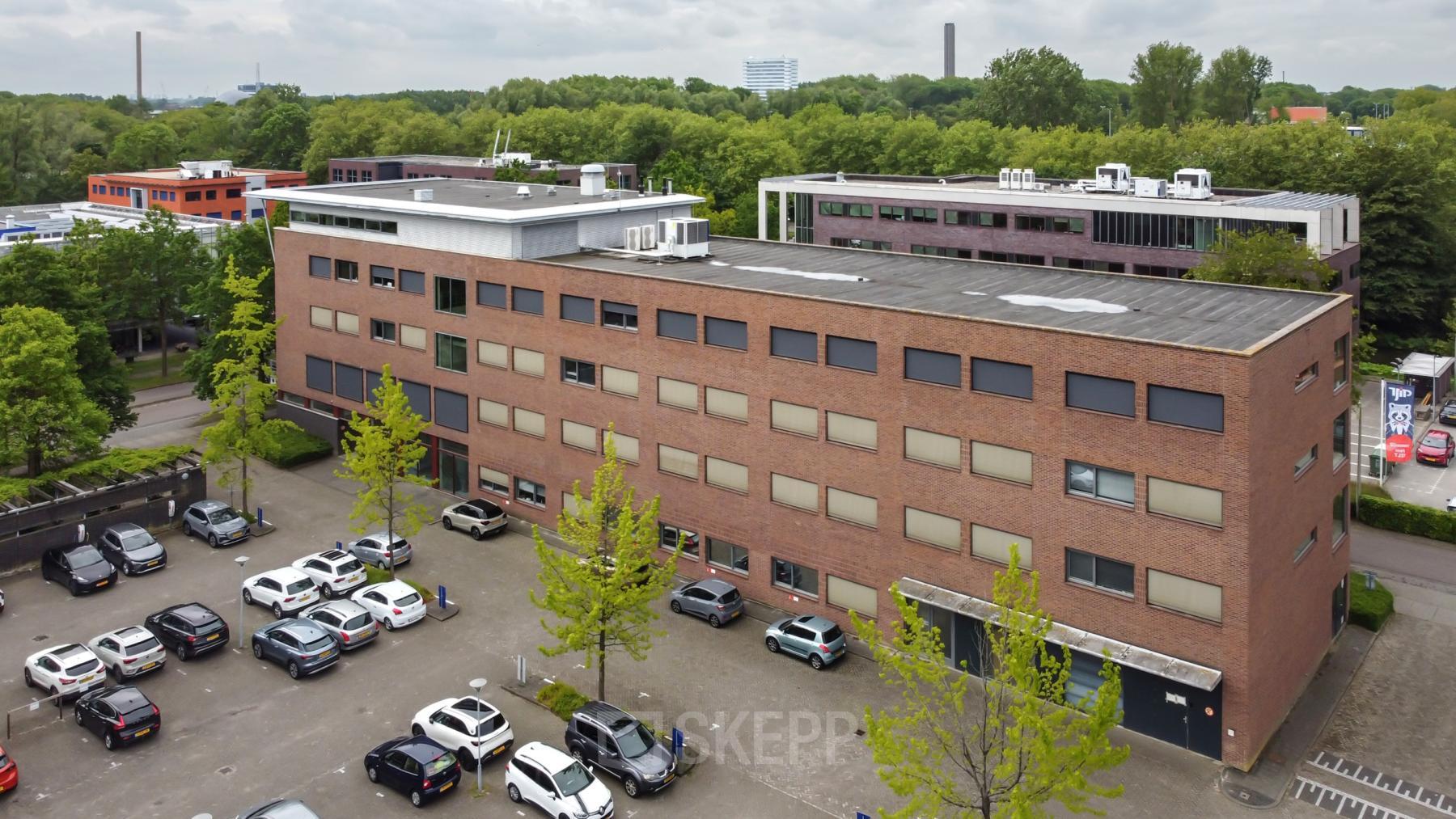 Buitenaanzicht van een kantoorpand op Delftechpark 9, Delft. Verschillende auto's geparkeerd op de parkeerplaats rondom het gebouw. Ideale plek voor kantoorruimte huren in Delft.