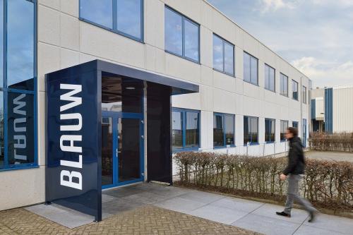 Kantoorpand aan de Europalaan 2 in Den Bosch met moderne gevel en glazen entree, gefotografeerd bij daglicht. Persoon loopt langs de ingang. Ideaal voor bedrijven die kantoorruimte willen huren.