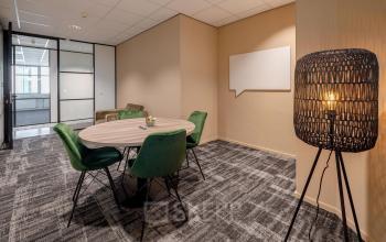 Een kantoorpand in Den Bosch met een vergaderruimte, voorzien van een ronde tafel en groene stoelen. De ruimte nodigt uit tot interactief overleg en is geschikt voor wie kantoorruimte wil huren.