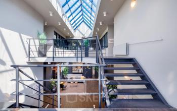 Dubbele verdieping in kantoorpand Europalaan 4, Den Bosch met een glazen dak, moderne trap en planten. Ideaal voor kantoorruimte huren met veel lichtinval en open indeling.
