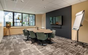 Vergaderruimte in kantoorpand met ovale tafel, groene stoelen, flip-over en tv-scherm. Gelegen op Europalaan 4 in Den Bosch. Ideaal voor bedrijven die kantoorruimte willen huren.