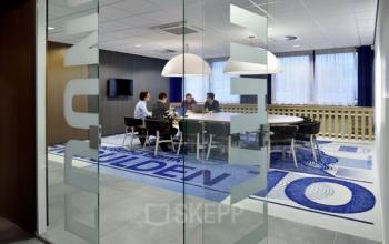 Vergaderruimte met glazen wanden op Amerikastraat 3, Den Bosch, waar mensen over zakelijke onderwerpen discussiëren rond een grote tafel.