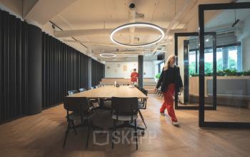 Moderne kantoorruimte huren in Den Bosch met tafels en stoelen, mensen voeren zakelijke activiteiten uit.