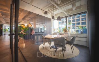 Moderne kantoorruimte huren in Den Bosch met een lichte vergaderruimte, voorzien van ronde tafel en comfortabele stoelen. Mensen aan het werk op laptops, met grote ramen voor natuurlijk licht.