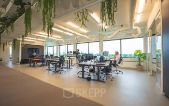 Modern kantoor op Hambakenwetering 1, Den Bosch, met open werkruimtes waar mensen zakelijk aan bureaus werken. Ideaal voor kantoorruimte huren, met ruime ramen en natuurlijke elementen.