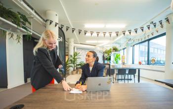 Gezellig kantoorpand op Hambakenwetering 1 in Den Bosch met moderne werkplekken, grote ramen en veel groen voor kantoorruimte huren. Twee zakelijke personen werken aan een tafel met laptop.