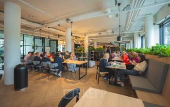 Kantoorruimte huren in Den Bosch met een moderne, gemeubileerde open werkvloer op Hambakenwetering 1, waar mensen geconcentreerd samenwerken en brainstormen aan tafels.