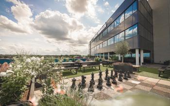 Kantoorruimte huren aan Hambakenwetering 1 in Den Bosch. Exterieur van modern kantoorpand met groen dakterras en schaakspel. Veel natuurlijke lichtinval en functionele buitenruimte voor ontspanning en zakelijke bijeenkomsten.