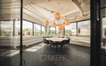 Licht en modern ingerichte vergaderruimte op Hambakenwetering 1, Den Bosch. Grote ramen, ronde tafel omringd door stoelen en opvallende hanglampen. Ideaal om kantoorruimte te huren.