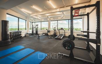 Fitnessruimte in een kantoorpand op Hambakenwetering 1, Den Bosch. Zicht op fitnessapparatuur en grote ramen met uitzicht. Ideaal voor ontspanning tijdens kantooruren. Geschikt voor bedrijven die kantoorruimte huren.