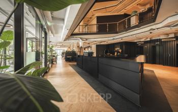 Moderne kantoorruimte huren aan de Hambakenwetering 1 in Den Bosch, met zwart interieur en houten vloeren, ingericht met balie en planten, biedt een warme en uitnodigende sfeer.