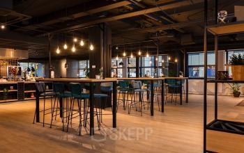 Moderne kantoorruimte huren in Den Bosch met hoge tafels en krukken, sfeervolle verlichting en een uitnodigende ambiance.