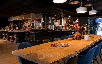 Gezellige kantoorruimte huren in Den Bosch met moderne keuken en lange houten tafel, ideaal voor vergaderingen.