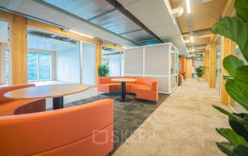 Moderne kantoorruimte te huur op Hambakenwetering 1-kr, Den Bosch: frisse inrichting met oranje banken en houten elementen. Gezellige sfeer, ideaal voor informeel overleg in een zakelijke omgeving.