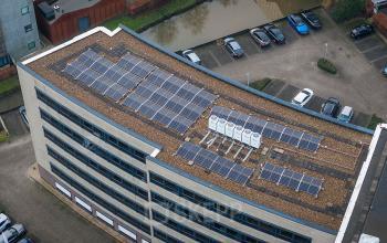 Luchtfoto van kantoorpand Pettelaarpark 110, Den Bosch, met zonnepanelen op het dak en een parkeerplaats vol auto's ernaast.