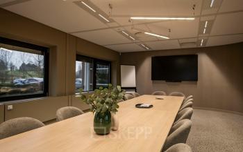 Kantoorruimte huren op Pettelaarpark 110, Den Bosch: stijlvol ingerichte vergaderruimte met grote houten tafel, comfortabele stoelen en moderne audiovisuele apparatuur. Grote ramen bieden veel natuurlijk licht en een inspirerend uitzicht.