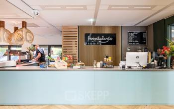 Gedeeltelijk groene receptieruimte van een kantoorpand op Pettelaarpark 110 in Den Bosch, met moderne meubels en een medewerker die bezig is achter de balie.