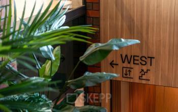 Ingang van een kantoorpand aan Hambakenwetering 5 in Den Bosch met houten afwerking en planten. Bordjes wijzen naar de westelijke vleugel.