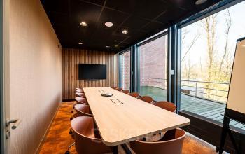 Vergaderruimte in kantoorpand op Hambakenwetering 5, Den Bosch met lange tafel, stoelen en scherm. Ideaal voor kantoorruimte huren.