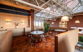 Gezellige kantoorruimte te huur in Den Bosch met houten tafels, stoelen en planten. Het pand heeft veel natuurlijk licht door de glazen dakconstructie.