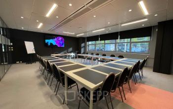 Kantoorruimte huren in Den Bosch, gelegen aan de Bruistensingel 500. Moderne vergaderruimte met lange tafels en scherm, voorzien van grote ramen voor natuurlijk licht.
