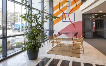 Moderne kantoorruimte huren op Bruistensingel 500, Den Bosch, met glazen wanden, kleurrijke muren en een chique glazen tafel, perfect voor creatieve meetings.