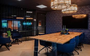 Moderne vergaderruimte in een kantoorpand op Reitschweg 1, Den Bosch, met houten tafel en blauwe stoelen onder stijlvolle verlichting.