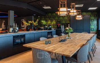 Kantoorruimte huren in Den Bosch aan de Reitschweg 1, met een stijlvolle keuken en eetruimte, voorzien van houten tafel en moderne stoelen, omgeven door zwarte kasten en sfeerverlichting.