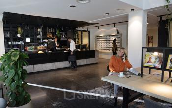 Moderne kantoorlounge met vrouw die telefoneert en persoon bij koffiebar in kantoorpand aan Koninginnegracht 19, Den Haag Centrum.