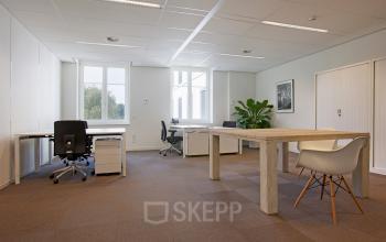 Moderne kantoorruimte met houten bureau en comfortabele stoelen op Koninginnegracht 19, ideaal voor ondernemers die een kantoor willen huren in Den Haag Centrum.