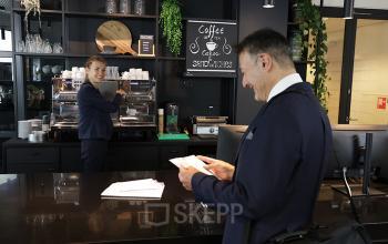 Professionele ontvangstbalie in kantoorpand aan Koninginnegracht 19, Den Haag Centrum, met barista en bezoeker.