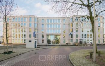 Het moderne kantoorpand op Alexanderveld 5-9 in Den Haag Centrum staat majestueus in de winterzon. Heldere glazen ramen reflecteren de lucht en omliggende bomen. Ideaal voor wie kantoorruimte wil huren in het centrum.