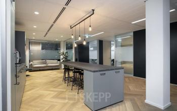 Moderne kantoorruimte met open vloerplan op Alexanderveld 5-9, Den Haag Centrum. Voorzien van een strak afgewerkte pantry met hoge tafel en krukken, geschikt voor informeel overleg of pauze.