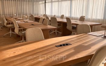 Lichte kantoorruimte in Den Haag Centrum met houten tafels en bureaustoelen, ideaal voor flexwerken of vergaderingen.