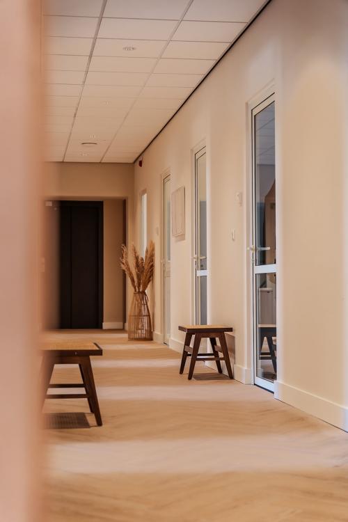 Lichte gang van een kantoorpand op Zeestraat 100, Den Haag Centrum met houten banken en glazen deuren.