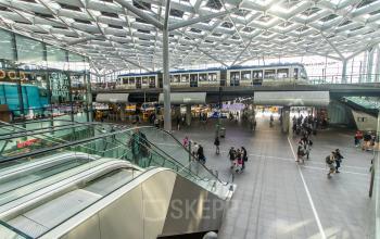 Een drukke binnenruimte bij Koningin Julianaplein 10 in Den Haag Centrum, met een trein bovenop, roltrappen en mensen die zich verplaatsen. Geschikt voor kantoorruimte huren.