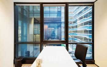 Kantoorruimte huren in Den Haag Centrum met een moderne werkplek voorzien van een groot raam met uitzicht op karakteristieke architectuur. De ruimte heeft een strakke inrichting met een tafel en stoel.