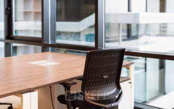 Moderne kantoorruimte huren in Den Haag Centrum, met grote ramen die veel natuurlijk licht binnenlaten. Voorzien van een bureau en stoel, geschikt voor productief werken.