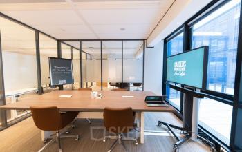Moderne kantoorruimte te huur in Den Haag Centrum op Anna van Buerenplein 41, met glazen wanden, een grote werktafel, comfortabele stoelen en presentatieschermen.