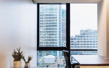 Lichte kantoorruimte aan Anna van Buerenplein 41 in Den Haag Centrum met uitzicht op de stad. Voorzien van een bureau met stoel en wat planten op de kast.