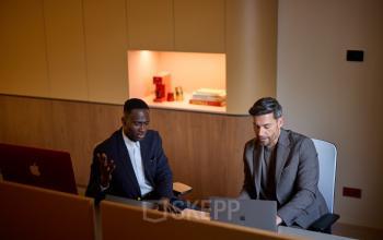 Twee mannen in een kantoorpand op Zeestraat 70, Den Haag Centrum, werkzaam op laptops in een moderne werkruimte.