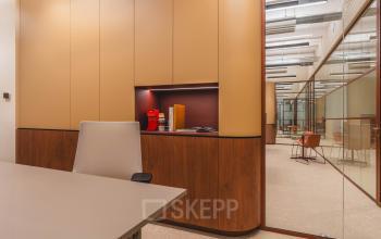 Moderne kantoorruimte huren op Zeestraat 70, Den Haag Centrum met strakke glazen wanden, houten kasten en een rode koffiemachine, ideaal voor professionele vergaderingen.